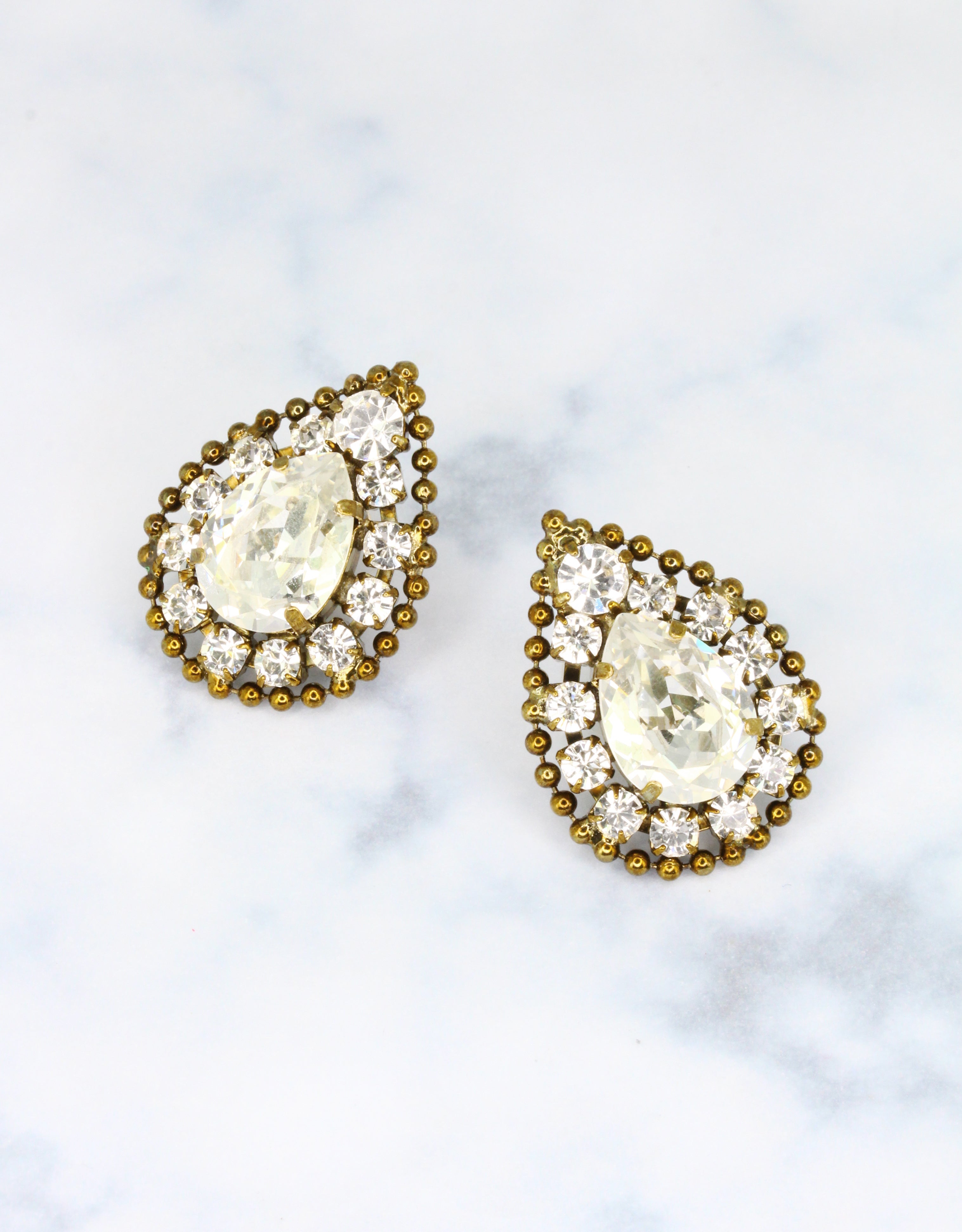 A pair of vintage earrings featuring a central round crystal surrounded by a teardrop-shaped crystal with smaller crystals in gold-tone settings.
