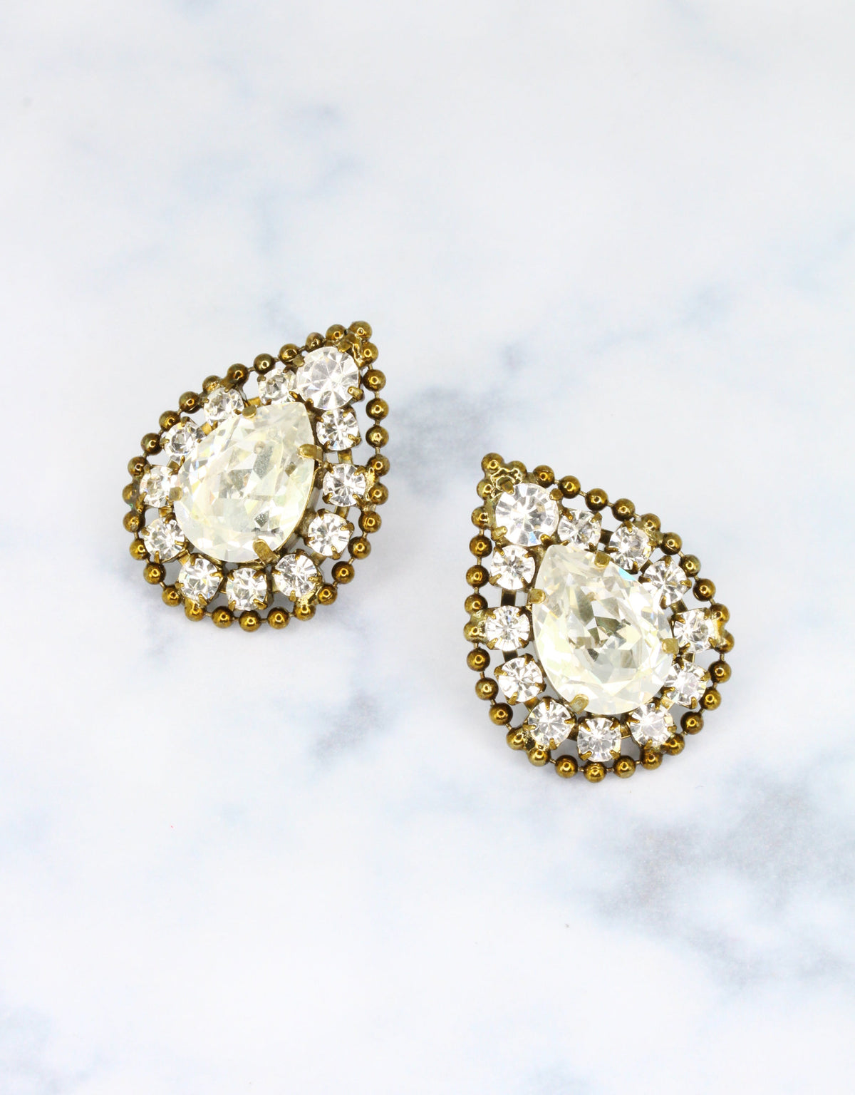 A pair of vintage earrings featuring a central round crystal surrounded by a teardrop-shaped crystal with smaller crystals in gold-tone settings.